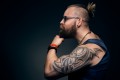 štúdiová fotka muža s výrazným tetovaním na ruke, držiaceho si rukou bradu
